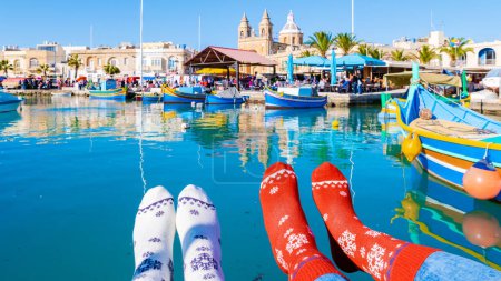 Photo for Colorful Christmas socks and Maltese fishing boats at the harbor of the village Marsaxlokk Malta, Marsaxlokk harbor fishing boats colorful Malta on a sunny day in winter - Royalty Free Image