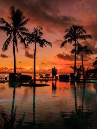 Photo for A young couple of men and women at a swimming pool during a vacation on a tropical island. man and woman in infinity pool during sunset. luxury vacation in Mauritius pool of a luxury pool villa - Royalty Free Image