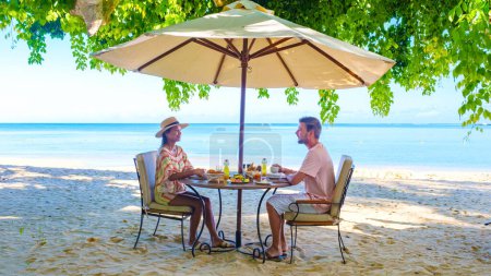 Téléchargez les photos : Homme et Femme prenant le petit déjeuner sur une plage tropicale à Maurice, un couple en vacances de lune de miel à Maurice - en image libre de droit