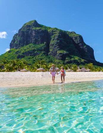 Foto de Hombre y mujer en una playa tropical en Mauricio, una pareja de vacaciones de luna de miel en Mauricio Le Morne Beach con Le Morne Mountain en el fondo con un cielo azul - Imagen libre de derechos