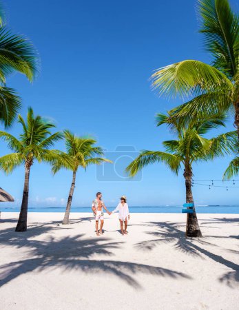 Foto de Hombre y mujer en una playa tropical con sillas de playa y palmeras en Mauricio, una pareja de vacaciones de luna de miel en Mauricio Le Morne Beach con Le Morne Mountain al fondo - Imagen libre de derechos