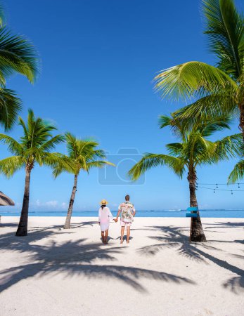 Foto de Hombre y mujer en una playa tropical con sillas de playa y palmeras en Mauricio, una pareja de vacaciones de luna de miel en Mauricio Le Morne Beach - Imagen libre de derechos