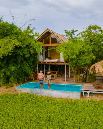 Téléchargez les photos : Un couple d'hommes et de femmes devant une ferme familiale de cabane de bambou, avec des rizières vertes en Thaïlande centrale avec un petit bassin plongeant donnant sur des rizières vertes - en image libre de droit