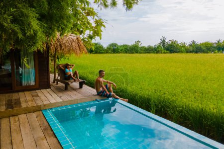 Photo for A couple of men and women in front of a Bamboo hut homestay farm, with Green rice paddy fields in Central Thailand with a small plunge pool looking out over green rice paddy fields - Royalty Free Image