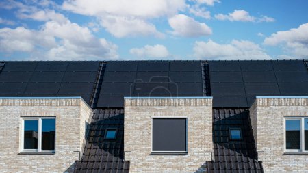 Foto de Casas de nueva construcción con paneles solares unidos en el techo contra un cielo soleado Primer plano de un edificio nuevo con paneles solares negros - Imagen libre de derechos