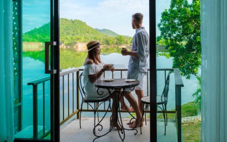 Photo for Couple on vacation in Thailand drinking coffee in the morning on their balcony looking out over a lake and mountains in central Thailand. - Royalty Free Image