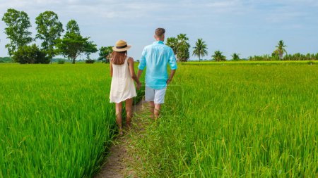 Foto de Un par de hombres y mujeres de vacaciones en Tailandia caminando por un sinuoso camino rural curvado en medio de arrozales de arroz verde en la región central de Tailandia Suphanburi, vista aérea de drones de arrozales verdes en Tailandia - Imagen libre de derechos