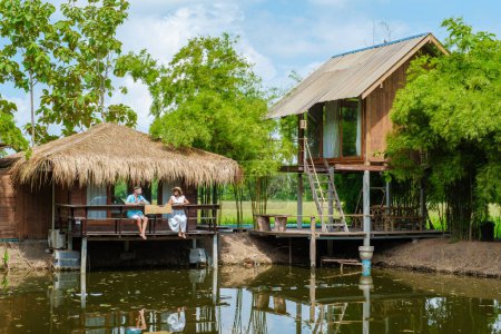 Téléchargez les photos : Couple d'hommes et de femmes dans une ferme de famille d'accueil de cabane de bambou avec des rizières vertes en Thaïlande centrale Suphanburi région, - en image libre de droit