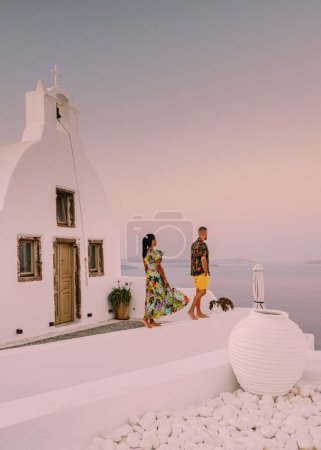 Photo for Santorini Greece, young couple on luxury vacation at the Island of Santorini watching sunrise by the blue dome church and whitewashed village of Oia Santorini Greece during sunrise during summer vacation - Royalty Free Image