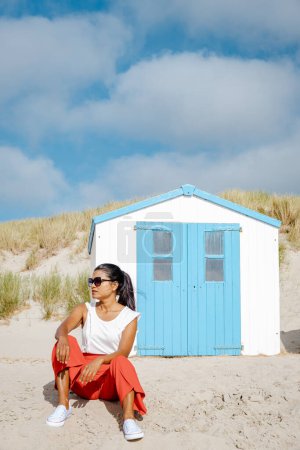 Téléchargez les photos : Femmes asiatiques visitant la plage de Texel avec en arrière-plan la maison bleue blanche sur la plage de Texel Pays-Bas, une cabane de plage sur l'île néerlandaise de Texel - en image libre de droit