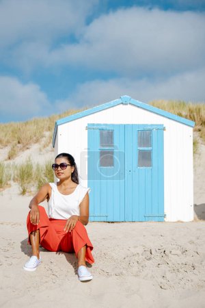 Téléchargez les photos : Femmes asiatiques visitant la plage de Texel avec en arrière-plan la maison bleue blanche sur la plage de Texel Pays-Bas, une cabane de plage sur l'île néerlandaise de Texel pendant l'été - en image libre de droit