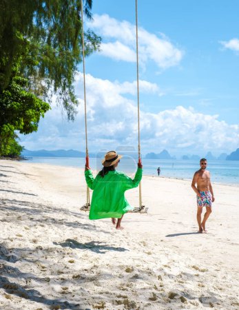 Téléchargez les photos : Un couple d'hommes et de femmes sur la plage de l'île tropicale de Naka près de Phuket Thaïlande, la femme à une balançoire sur la plage. Île de Naka Phuket Thaïlande - en image libre de droit