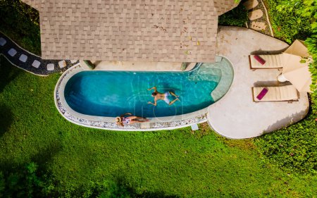 Foto de Vista superior del dron de un par de hombres europeos y una mujer asiática en una piscina infinita en Tailandia, unas vacaciones de lujo en Tailandia, una villa de piscina privada en una isla tropical cerca de Phuket - Imagen libre de derechos