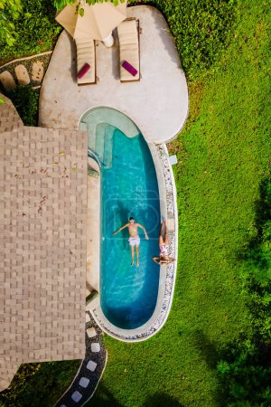 Photo for Drone top view of a couple of European men and an Asian woman in an infinity pool in Thailand, a luxury vacation in Thailand, a private pool villa on a tropical Island near Phuket - Royalty Free Image
