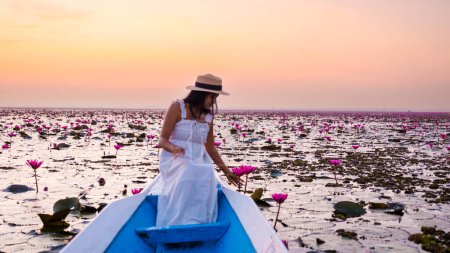 Photo for Asian women with a hat and dress in a boat at the Beautiful Red Lotus Sea Kumphawapi is full of pink flowers in Udon Thani in northern Thailand. Flora of Southeast Asia. - Royalty Free Image