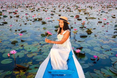 Foto de Asian women with a hat and dress in a boat at the Beautiful Red Lotus Sea Kumphawapi is full of pink flowers in Udon Thani in northern Thailand. Flora of Southeast Asia. - Imagen libre de derechos