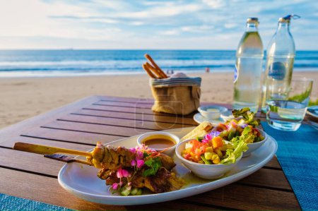 Téléchargez les photos : Nourriture thaïlandaise sur une table sur la plage en Thaïlande. table avec cuisine thaïlandaise Thai sate - en image libre de droit