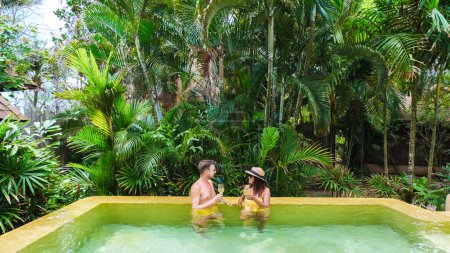 Téléchargez les photos : Un couple d'hommes et de femmes en vacances de luxe en Thaïlande dans un complexe 5 étoiles relaxant dans la piscine d'une villa de luxe en Thaïlande - en image libre de droit