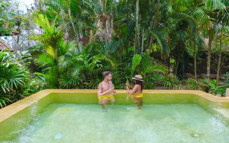 Téléchargez les photos : Un couple d'hommes et de femmes en vacances de luxe en Thaïlande dans un complexe 5 étoiles relaxant dans la piscine maison moderne avec une piscine par une journée ensoleillée dans la forêt verte de la jungle - en image libre de droit