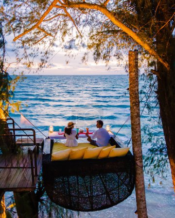Téléchargez les photos : Dîner romantique sur la plage à Koh Kood Thaïlande, un couple d'hommes et de femmes dînant sur la plage haut dans l'arbre à un nid d'oiseaux en Thaïlande pendant le coucher du soleil à Ko Kut Trat - en image libre de droit