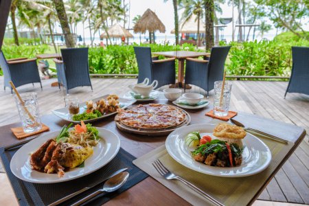 Téléchargez les photos : Table avec pizza et cuisine thaïlandaise sur la plage en Thaïlande, près de la table du dîner au coucher du soleil - en image libre de droit
