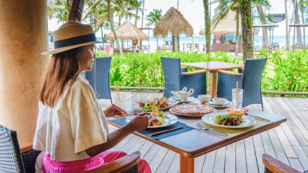 Téléchargez les photos : Femme asiatique ayant table de petit déjeuner sur la plage de Koh Kood en Thaïlande, table de petit déjeuner dans un hôtel de luxe - en image libre de droit