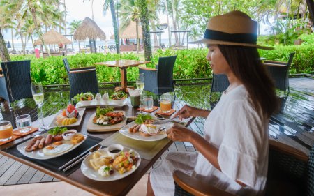Photo for Asian woman having breakfast table on the beach of Koh Kood in Thailand, breakfast table at a luxury hotel - Royalty Free Image