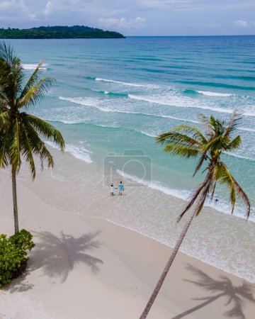 Téléchargez les photos : Un couple d'hommes et de femmes marchant à White Beach Koh Kood Island Thaïlande Trat, drone vue aérienne de la plage tropicale avec des palmiers suspendus et une turque couleur océan par une journée ensoleillée pendant les vacances - en image libre de droit