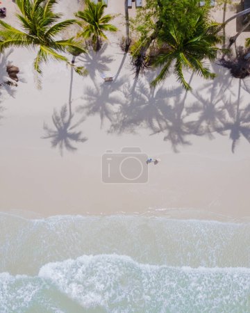 Foto de Un par de hombres y mujeres caminando en White Beach Koh Kood Island Thailand Trat, vista aérea de drones de una playa tropical con palmeras colgantes y un océano de color turquesa en un día soleado, Ko Kut Island - Imagen libre de derechos