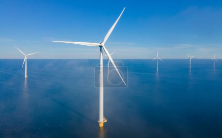 Foto de Parque de molinos de viento con nubes de niebla colgantes bajas y un cielo azul, parque de molinos de viento en la vista aérea del océano con turbina eólica Flevoland Países Bajos Ijsselmeer. Producción de energía verde en los Países Bajos - Imagen libre de derechos