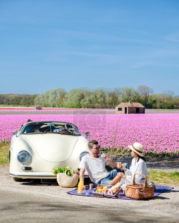 Photo for Lisse Netherlands couple doing a road trip with an old vintage car in the Dutch flower bulb region with tulip fields during Spring - Royalty Free Image