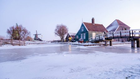 Photo for Dutch historical village Zaanse Schans Netherlands a Dutch windmill village during sunrise at winter with ice and snow and frozen canal - Royalty Free Image