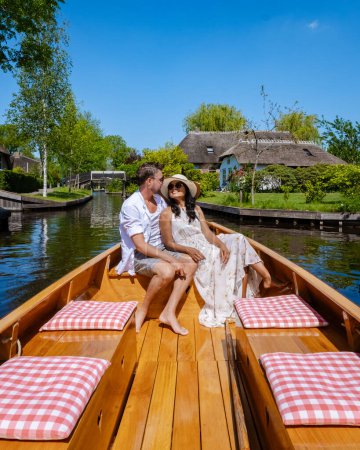 Foto de Joven pareja diversa visita Giethoorn Países Bajos pareja visita el pueblo con un barco, vista del famoso pueblo con canales y casas de techo de paja rústica - Imagen libre de derechos