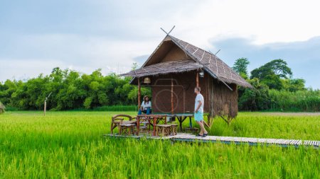 Photo for A couple of men and woman at a small homestay at the farm with a green rice paddy field in Central Thailand - Royalty Free Image