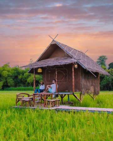 Téléchargez les photos : Un couple d'hommes et de femmes dans une petite famille d'accueil sur la ferme avec une rizière verte en Thaïlande centrale, jeune couple en vacances à la campagne thaïlandaise - en image libre de droit