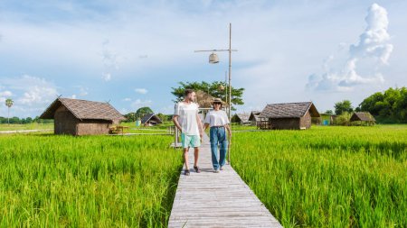 Foto de Un par de hombres y mujeres en una pequeña casa de familia en la granja con un arrozal de arroz verde en el centro de Tailandia, pareja joven de vacaciones en el campo tailandés - Imagen libre de derechos