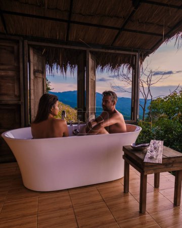 Foto de Un par de hombres y mujeres en una bañera con vistas a las montañas de Chiang Rai norte de Tailandia durante las vacaciones. Baño exterior, bañera al atardecer - Imagen libre de derechos