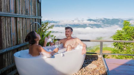 Téléchargez les photos : Un couple mixte d'hommes et de femmes dans une baignoire donnant sur les montagnes de Chiang Rai Nord de la Thaïlande pendant les vacances. Salle de bains extérieure, baignoire au coucher du soleil - en image libre de droit