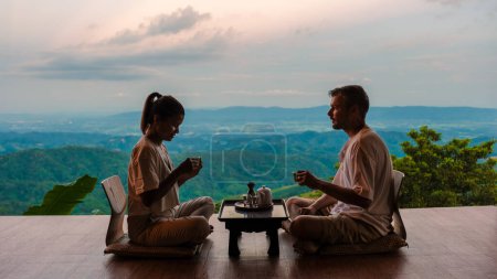Téléchargez les photos : Un couple d'hommes et de femmes buvant du thé dans les montagnes du nord de la Thaïlande au balcon d'une cabane en bois - en image libre de droit