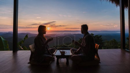 Téléchargez les photos : Un couple d'hommes et de femmes buvant du thé dans une famille d'accueil de style japonais en vacances dans le nord de la Thaïlande, séjournant dans une cabane chez l'habitant dans les montagnes de Chiang Rai Doi Chang - en image libre de droit
