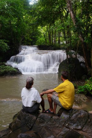 Téléchargez les photos : Cascade de forêt profonde en Thaïlande. Chute d'eau Erawan dans le parc national. un couple d'hommes et de femmes se relaxant dans la forêt de jungle lors d'un voyage en visitant la nature avec la forêt et les cascades - en image libre de droit