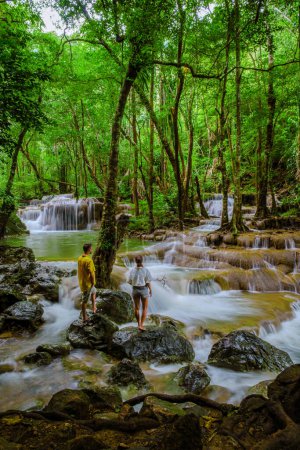 Téléchargez les photos : Erawan Waterfall Thailand, une belle cascade de forêt profonde en Thaïlande. Chute d'eau Erawan dans le parc national. un couple d'hommes et de femmes en voyage dans la nature avec forêt et cascades - en image libre de droit