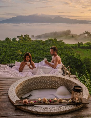 Photo for A couple of men and women in a bathtub looking out over the mountains of Northern Thailand during vacation. Outdoor bathroom, and bathtub during sunset at the mountains with mist and fog - Royalty Free Image