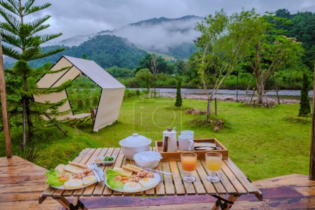 Téléchargez les photos : Petit déjeuner dans les montagnes du nord de la Thaïlande. Petit déjeuner américain et thaïlandais avec soupe de riz, saucisses et pain - en image libre de droit