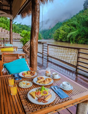 Téléchargez les photos : Table de petit déjeuner dans une maison de plage tropicale sur la rivière Kwai en Thaïlande.Maison de radeau flottant en bois dans la rivière Kwai Kanchanaburi, Thaïlande, petit déjeuner avec œufs pain et café - en image libre de droit