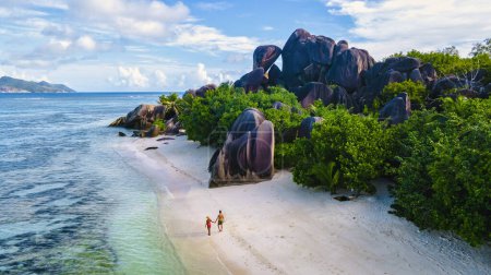 Foto de Anse Source dArgent beach, La Digue Island, Seychelles, un par de hombres y mujeres en la playa durante el atardecer, vacaciones de lujo en las Seychelles en una playa tropical blanca con océano de color turquesa - Imagen libre de derechos