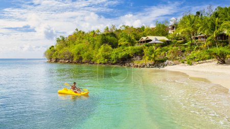 Foto de Jóvenes en un kayak en una isla tropical en el Mar Caribe, Santa Lucía o Santa Lucía. joven de vacaciones en una isla tropical remando frente a la playa con el océano de color turquesa - Imagen libre de derechos