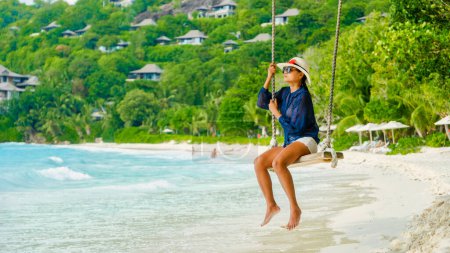 Téléchargez les photos : Jeunes femmes à la balançoire sur une plage tropicale des îles Mahe Tropical Seychelles. femme regardant au-dessus de l'océan depuis une balançoire à la plage aux Seychelles - en image libre de droit