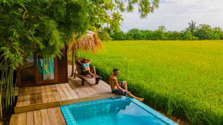 Téléchargez les photos : Un couple d'hommes et de femmes devant une ferme de famille d'accueil de cabane de bambou, avec des rizières vertes en Thaïlande centrale avec un petit bassin profond - en image libre de droit