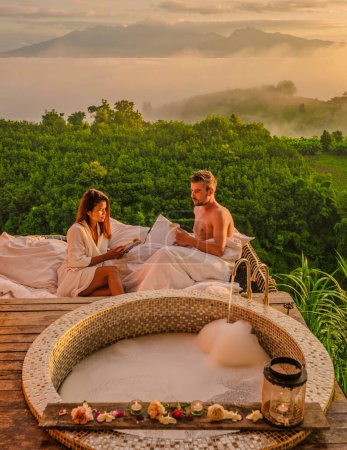 Photo for A couple of men and women in a bathtub looking out over the mountains of Northern Thailand during vacation. Outdoor bathroom, and bathtub during sunset at the mountains with mist and fog - Royalty Free Image